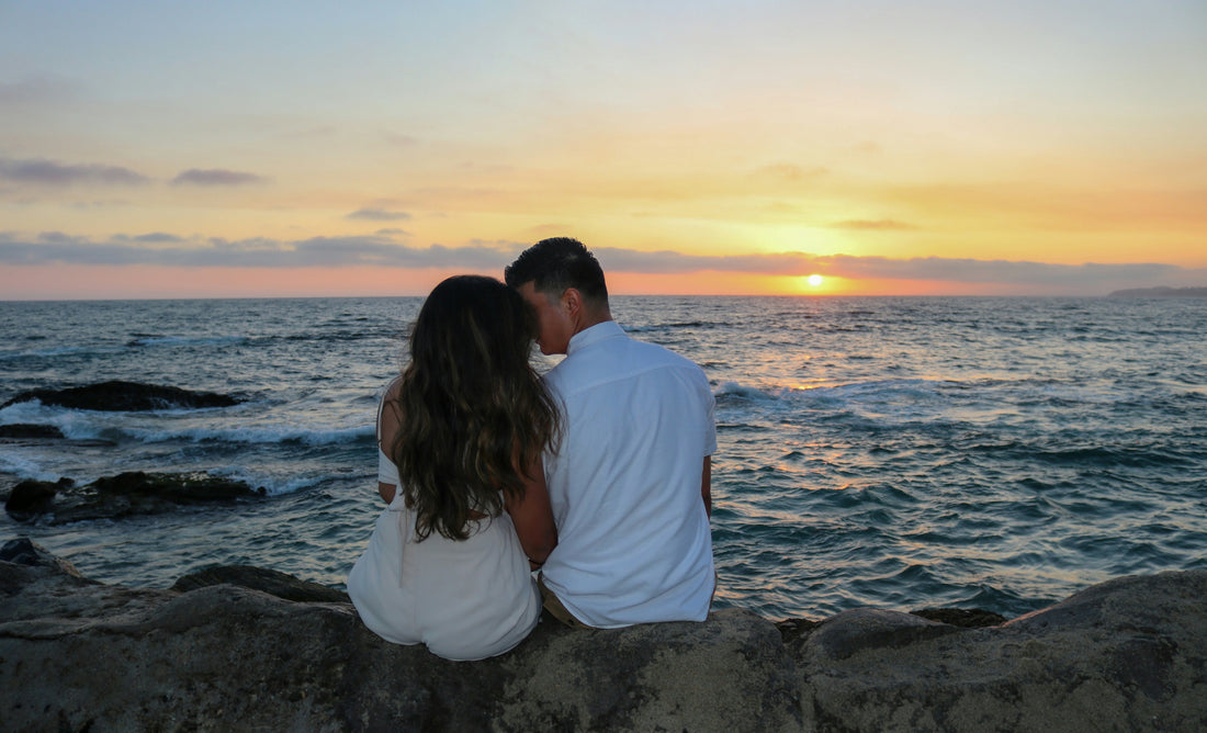 a man and a woman sitting on a rock near the ocean