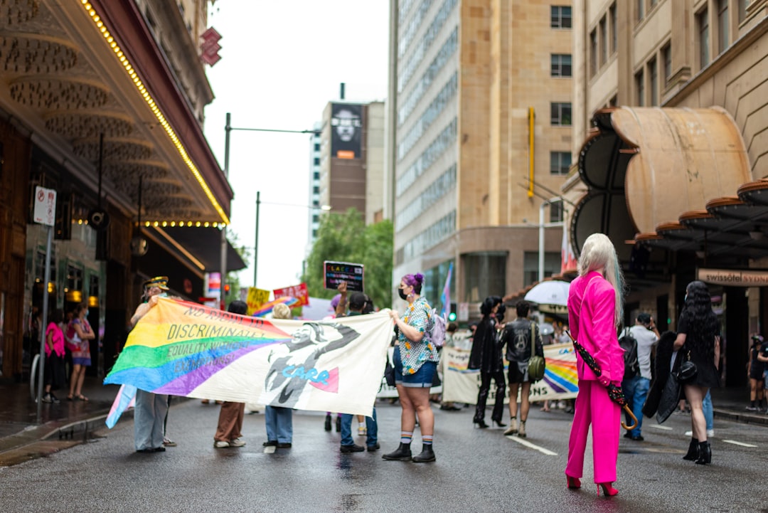 a-group-of-people-walking-down-a-street-holding-a-rainbow-flag-Bn-tqgtX_KI