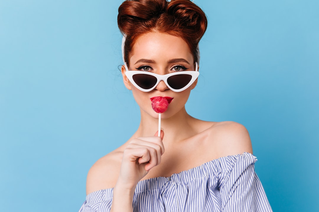 a-woman-wearing-sunglasses-holding-a-lollipop-in-front-of-her-face-uPecRcU1T4Q