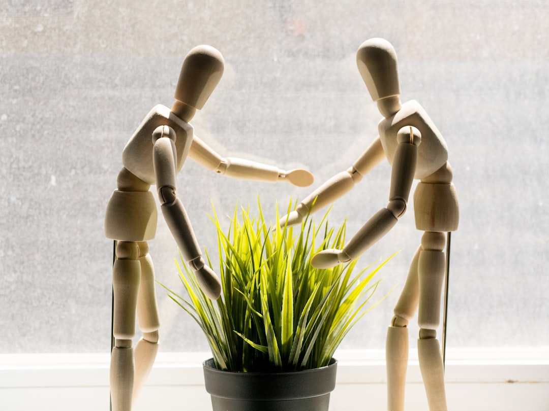 two-wooden-mannequins-reaching-towards-a-potted-plant-iUUPxaXbJp0